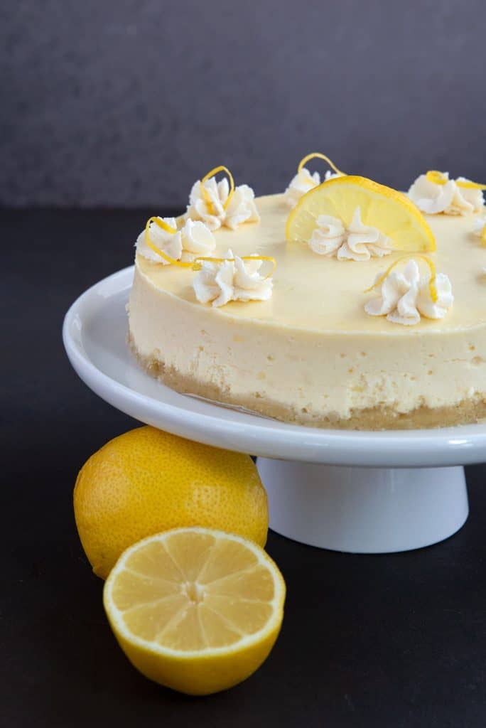 Keto Lemon Cheesecake on a white cake plater with lemons beside it.