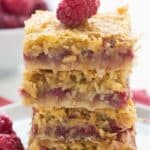 Titled image of a stack of keto raspberry coconut bars on a white plate over a pink napkin.