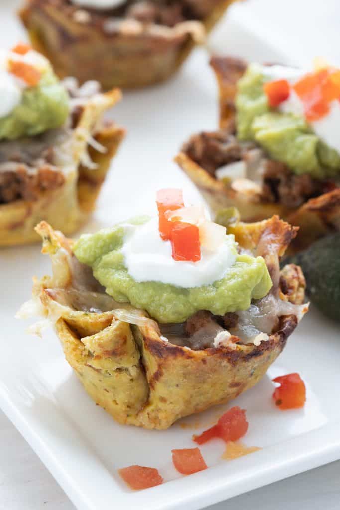 Keto taco cups on a white platter, topped with guacamole and sour cream.