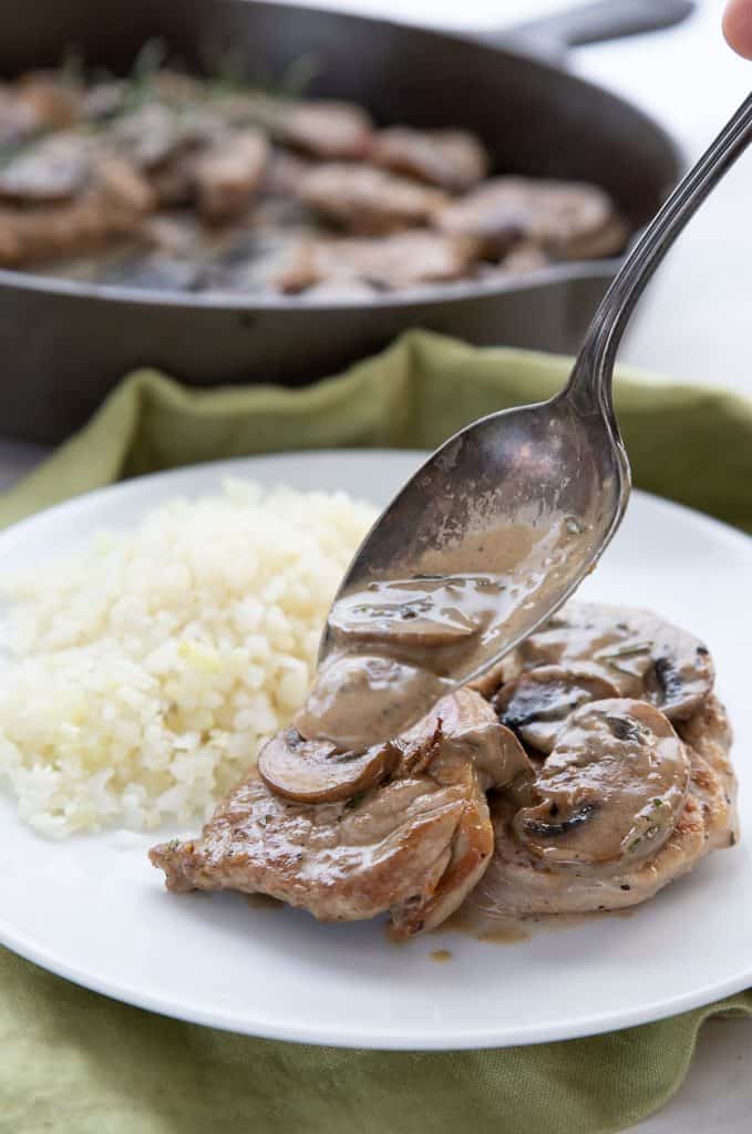 A spoon pouring mushroom rosemary sauce over pork medallions on a white plate.