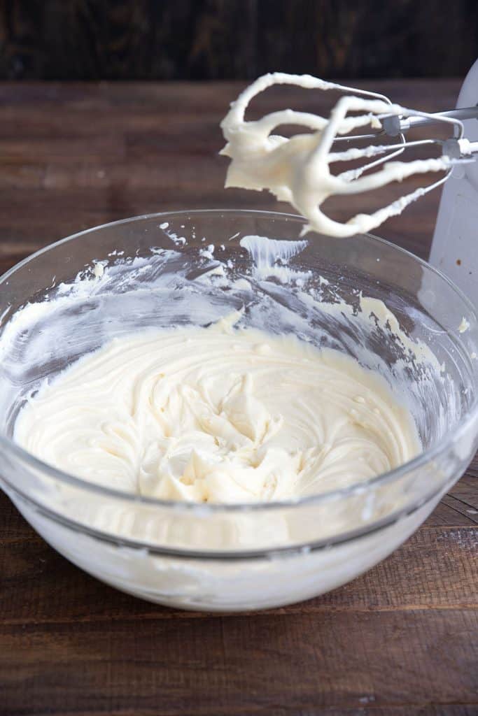 A bowl of keto cream cheese frosting with beaters sitting above it.