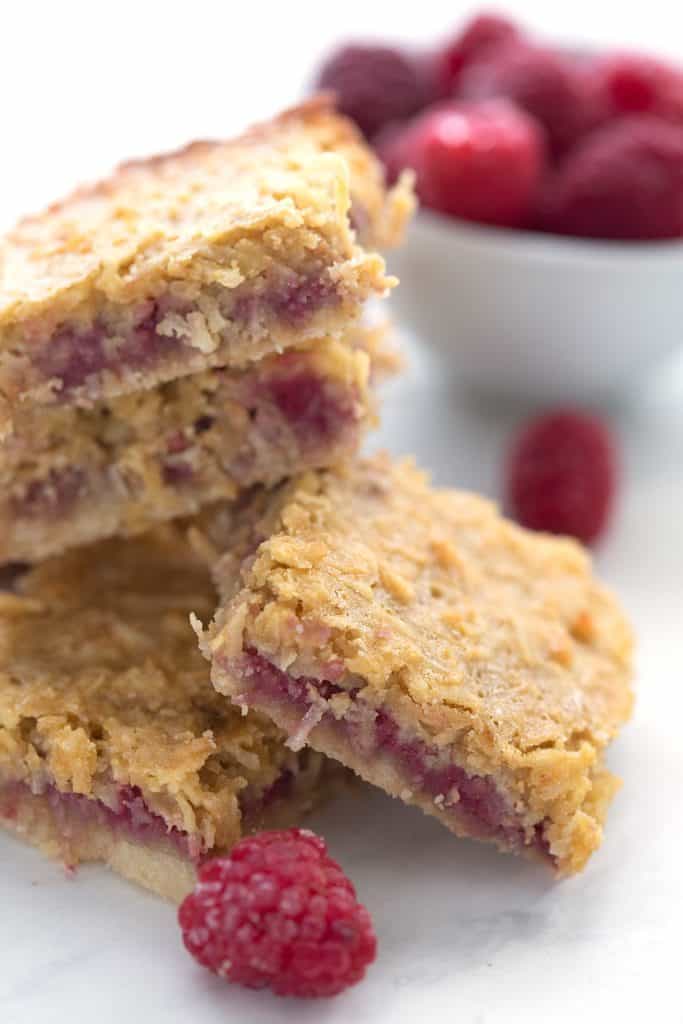A pile of raspberry coconut bars with a bowl of berries in the background.