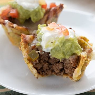 Close up shot of keto taco cups on a white plate with a bite taken out of the front one.