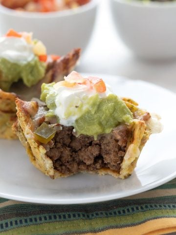 A keto taco cup with guacamole and sour cream on a white plate over a colourful napkin.