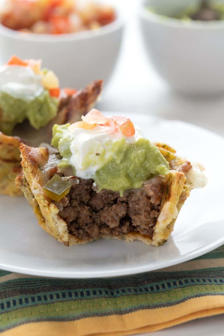 A keto taco cup with guacamole and sour cream on a white plate over a colourful napkin.