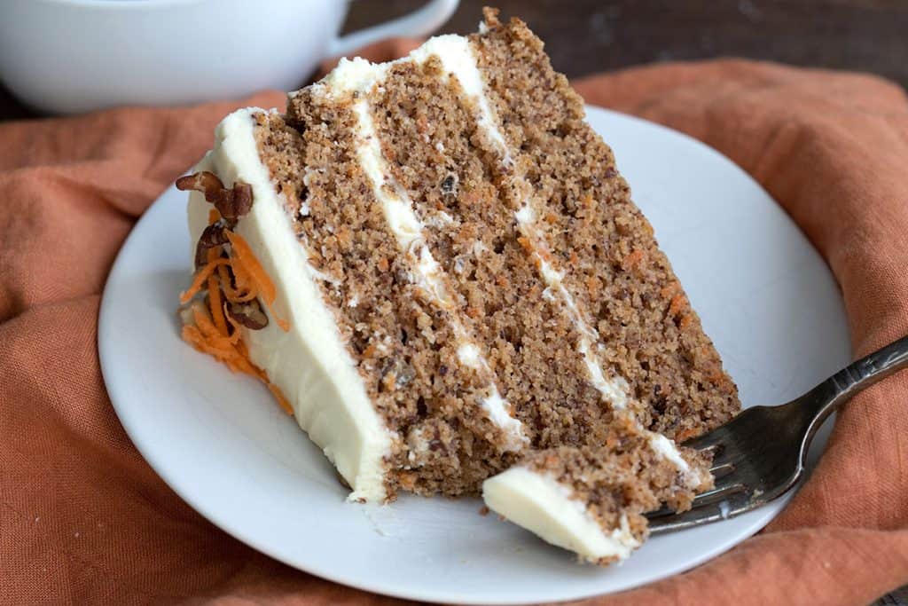 Close up shot of a slice of keto carrot cake on a white plate over an orange napkin.
