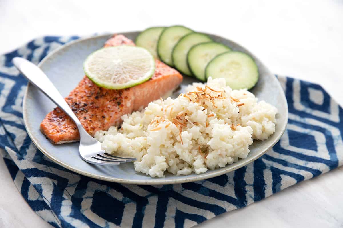 Close up shot of plate filled with coconut cauliflower rice, salmon, and cucumber over a blue patterned napkin