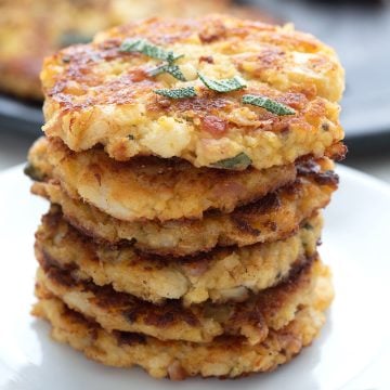 A stack of cauliflower fritters on a white plate with chopped sage on top.