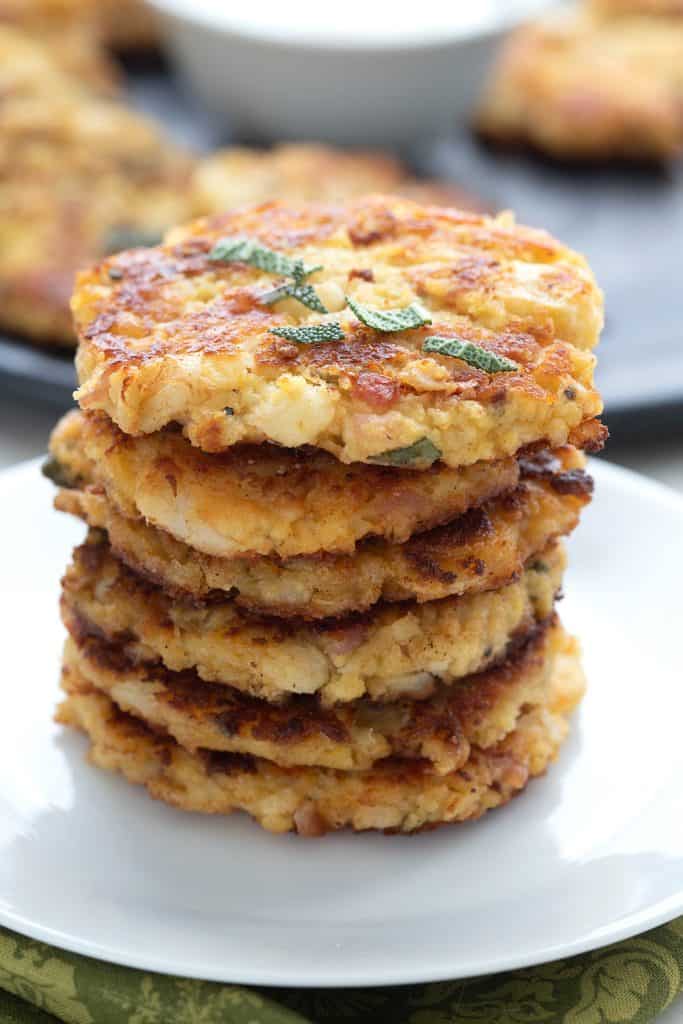 A stack of cauliflower fritters on a white plate with chopped sage on top.