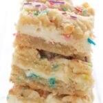 Titled image of a stack of Keto Sugar Cookie Cheesecake Bars on a white background.