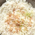 Top down image of a metal pan filled with coconut cauliflower rice, with shredded coconut and lime zest on top.