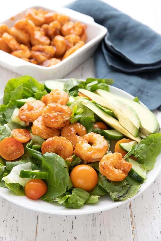 Green salad with topped with Keto Buffalo Shrimp on a white plate with a blue napkin in the background.