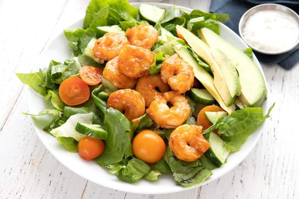 A white plate filled with salad, topped with Buffalo Shrimp.
