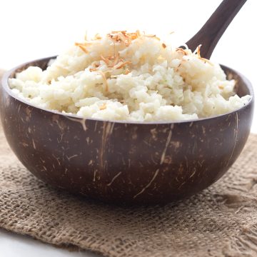 A brown wooden bowl filled with coconut cauliflower rice over a burlap napkin.