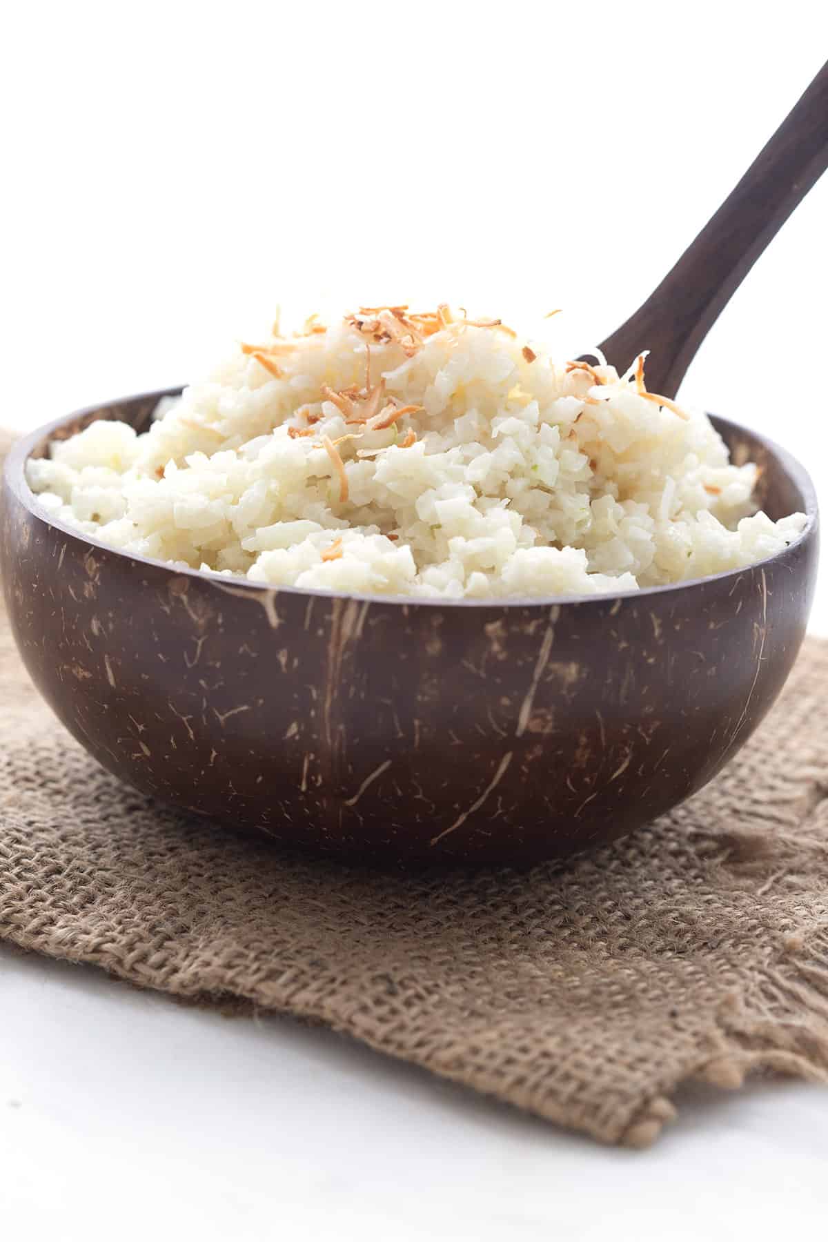 A brown wooden bowl filled with coconut cauliflower rice over a burlap napkin.
