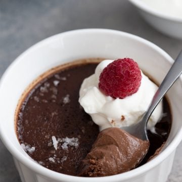 A spoon digging into a chocolate keto pot de creme with raspberries on top.