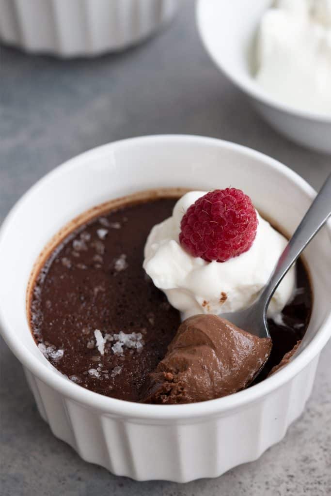 A spoon digging into a chocolate keto pot de creme with raspberries on top.