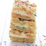 A stack of keto sugar cookie cheesecake bars on a white table, with sprinkles strewn around.