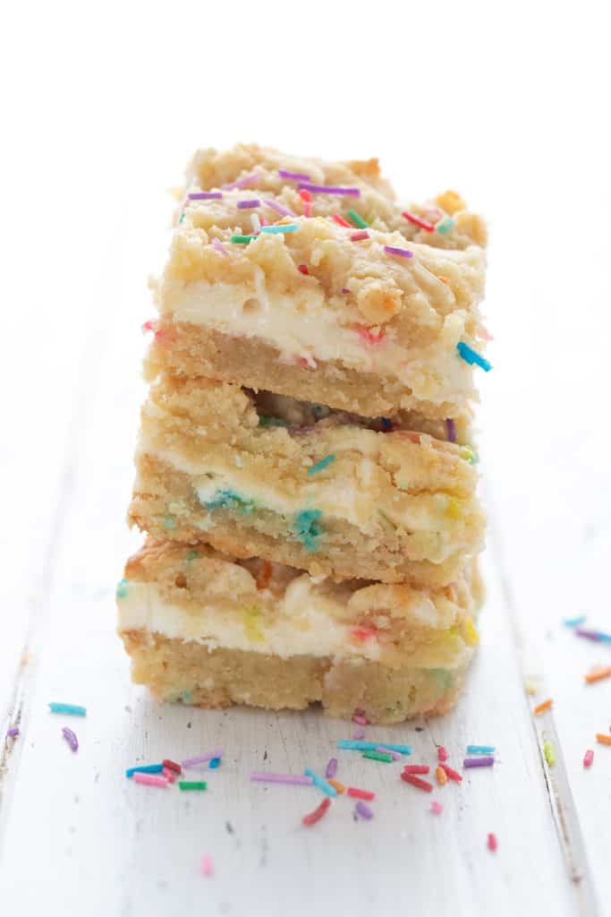A stack of keto sugar cookie cheesecake bars on a white table, with sprinkles strewn around.