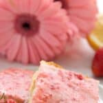 Titled image of Keto Strawberry Lemon Blondies on a whit plate in front of pink Gerbera daisies.