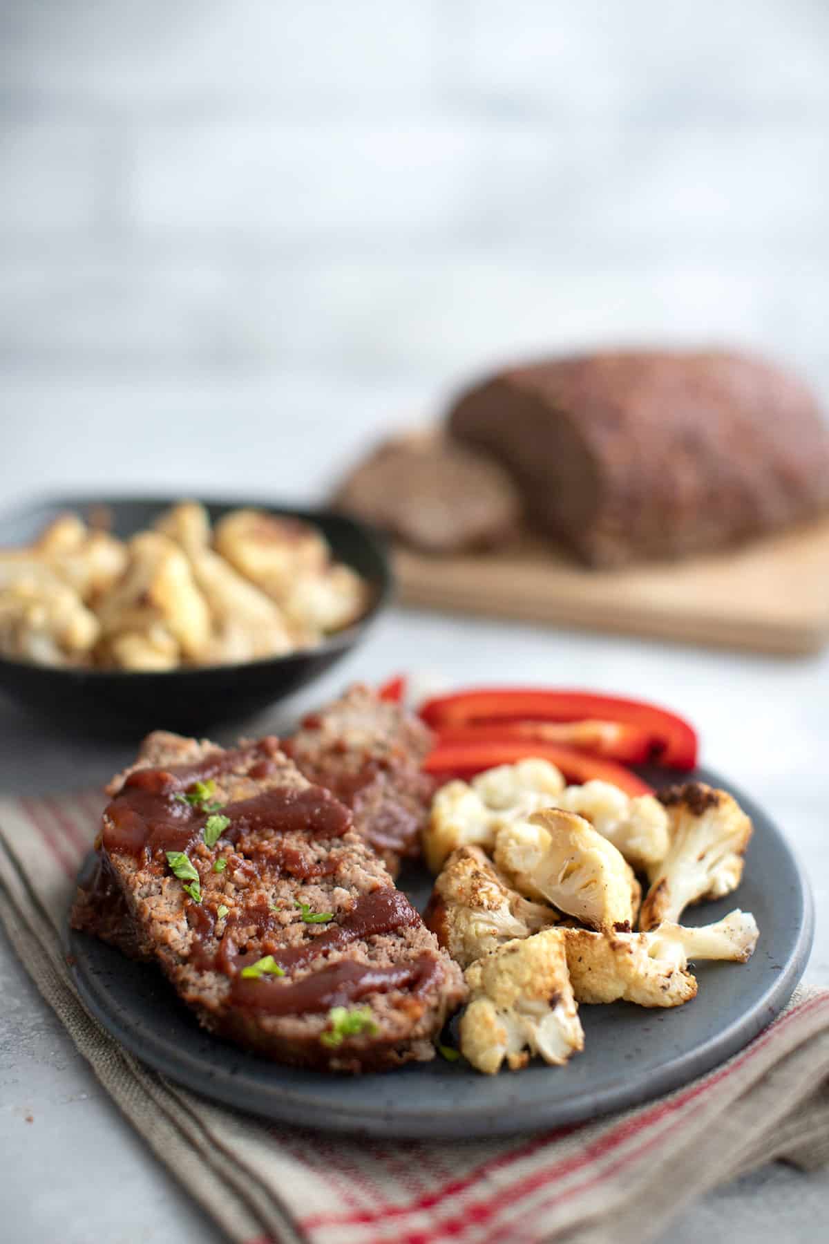A grey plate filled with slices of slow cooker keto meatloaf, with roasted cauliflower and red peppers as well.