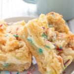 Titled image of two Keto Sugar Cookie Cheesecake Bars on a white plate over a colorful napkin.