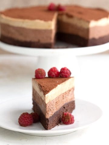 A slice of keto mousse cake on a white plate with the rest of the cake in the background.