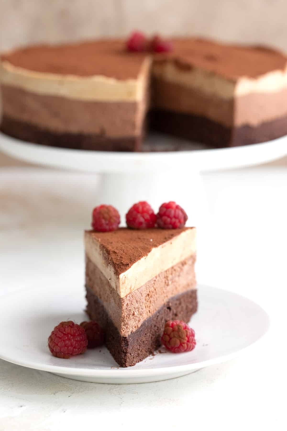 A slice of keto mousse cake on a white plate with the rest of the cake in the background.