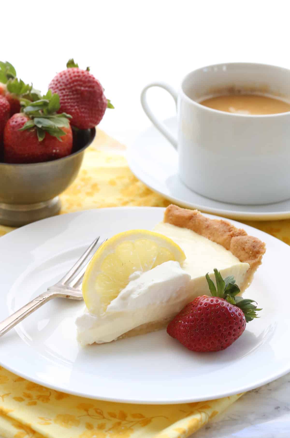 A slice of lemon sour cream pie on a white plate with a strawberry.