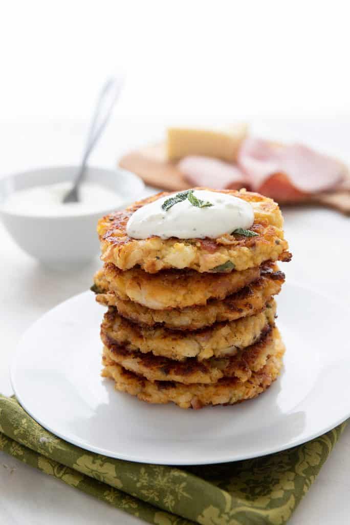 A stack of cauliflower fritters with a dollop pf ranch dressing on top, sitting on a white plate over a green napkin.