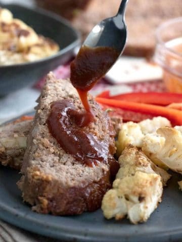 A spoon drizzling sugar free bbq sauce over a slice of keto meatloaf.