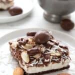 A keto almond joy cheesecake bar on a white plate with almonds and coconut shreds.