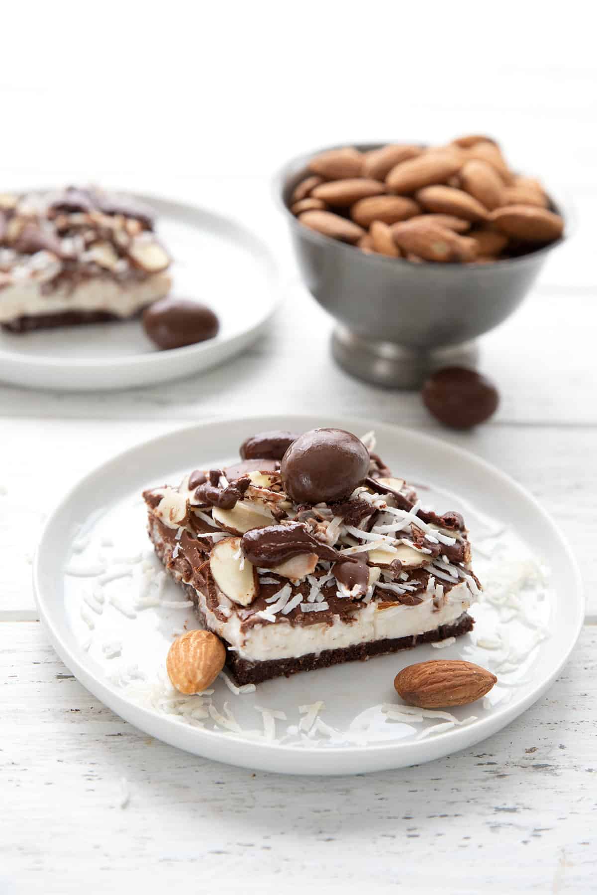 A no bake keto cheesecake bar on a white plate with a bowl of almonds in the background.