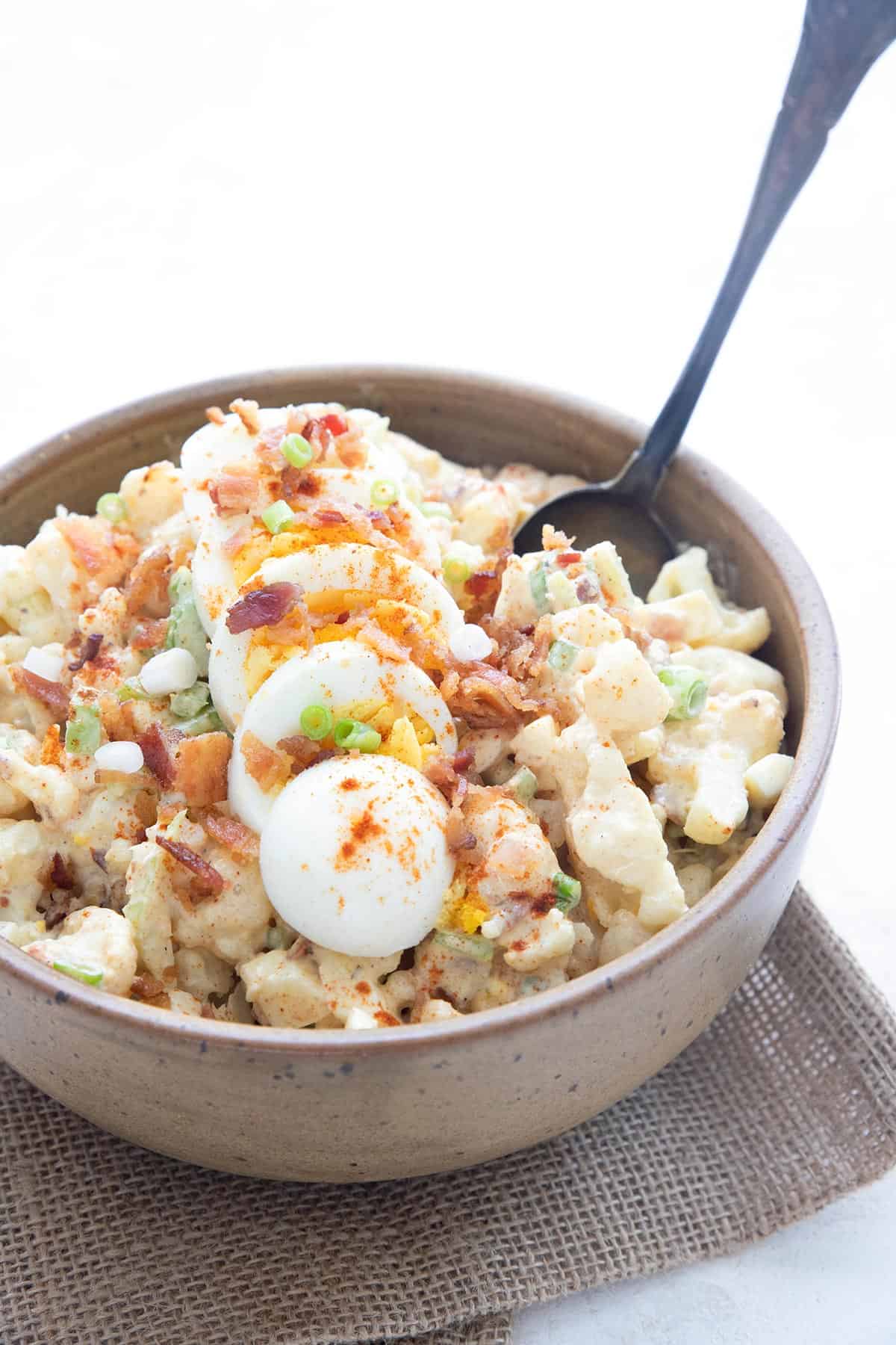 A bowl filled with keto cauliflower salad, with a serving spoon sticking out of it.