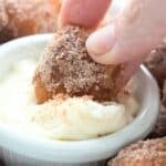 Close up shot of a hand dipping a keto cinnamon pretzel bites into sweetened cream cheese.