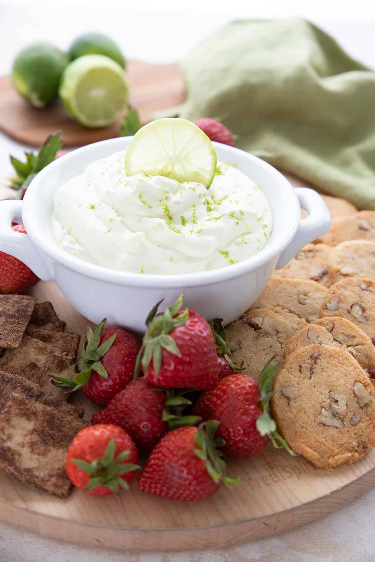 A white bowl filled with key lime cheesecake dip, surrounded by strawberries, cookies, and crackers for dipping.