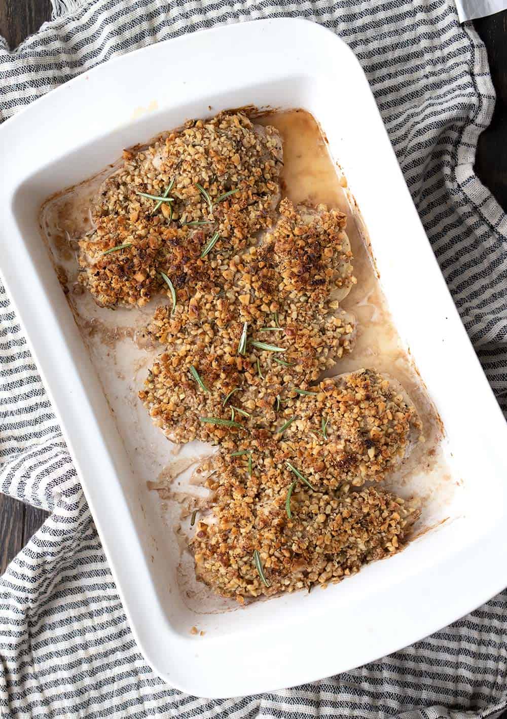 A white pan filled with walnut crusted chicken breasts over a striped grey and white cloth.