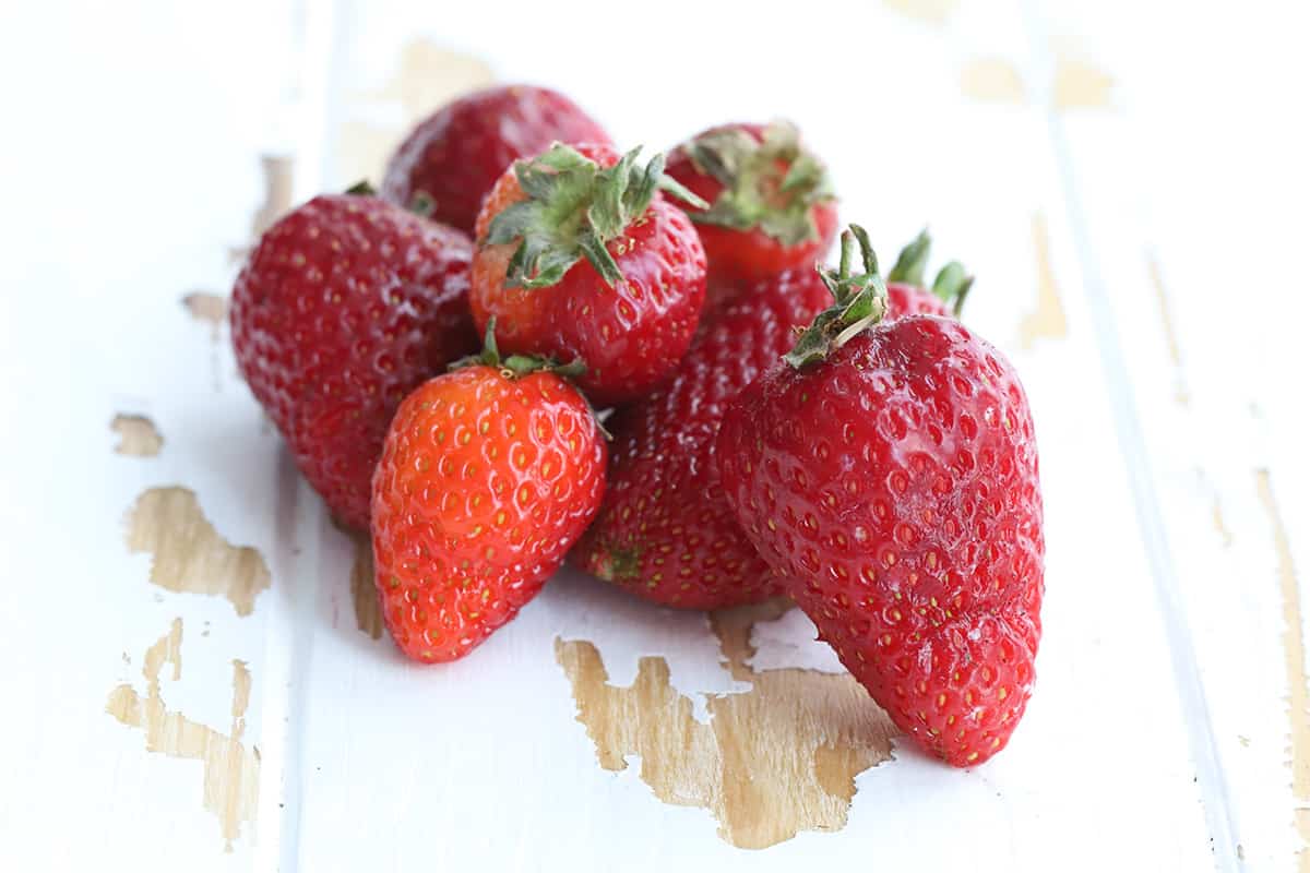 A pile of fresh strawberries on a rustic wooden table.