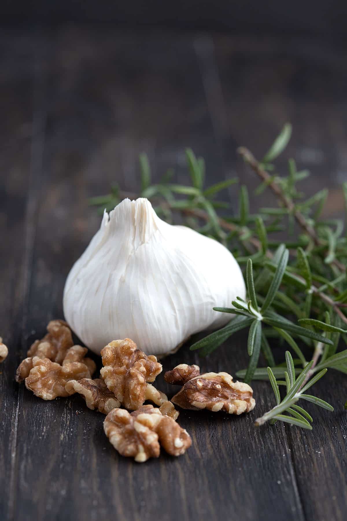 Walnuts, rosemary, and garlic on a brown wooden table.