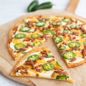 Jalapeno Popper Pizza on a wooden pizza board, with a slice taken out of it.