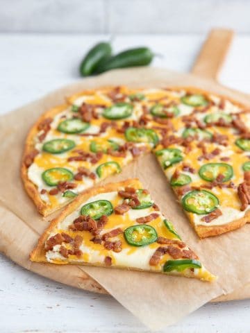 Jalapeno Popper Pizza on a wooden pizza board, with a slice taken out of it.