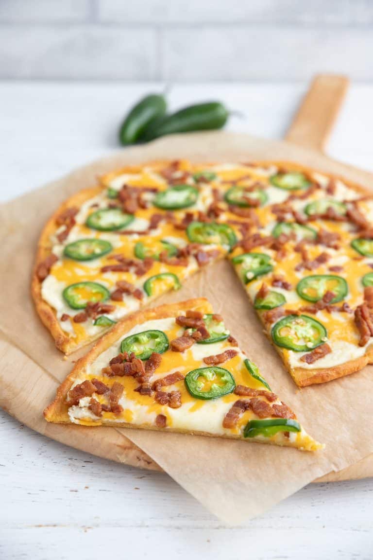 Jalapeno Popper Pizza on a wooden pizza board, with a slice taken out of it.