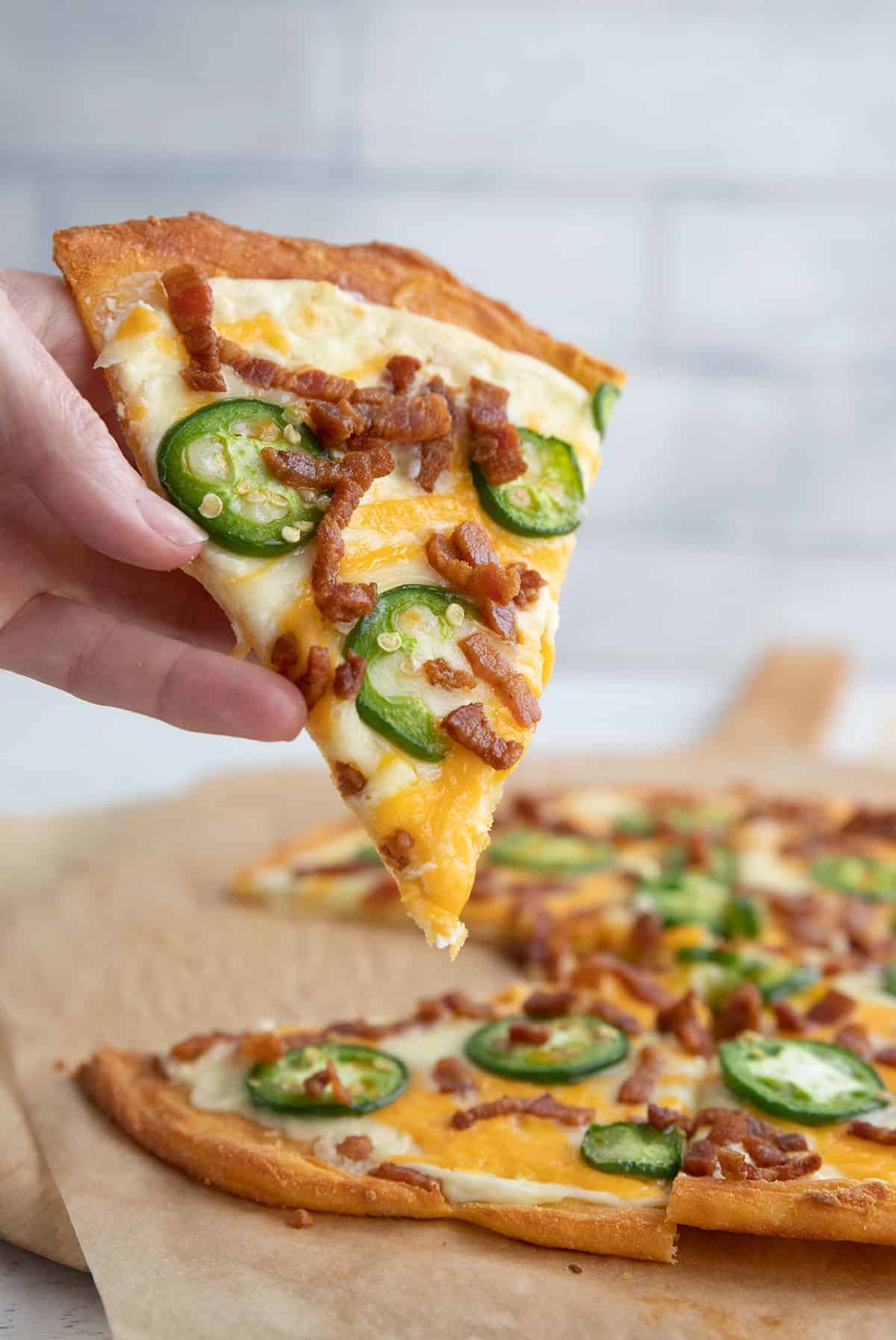 A hand lifting a slice of Jalapeno Popper Pizza out of the main pizza.