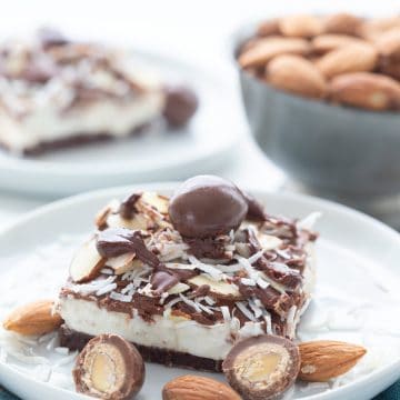 A keto no bake cheesecake bar on a white plate, over a teal napkin, with sugar-free chocolate covered almonds around it.