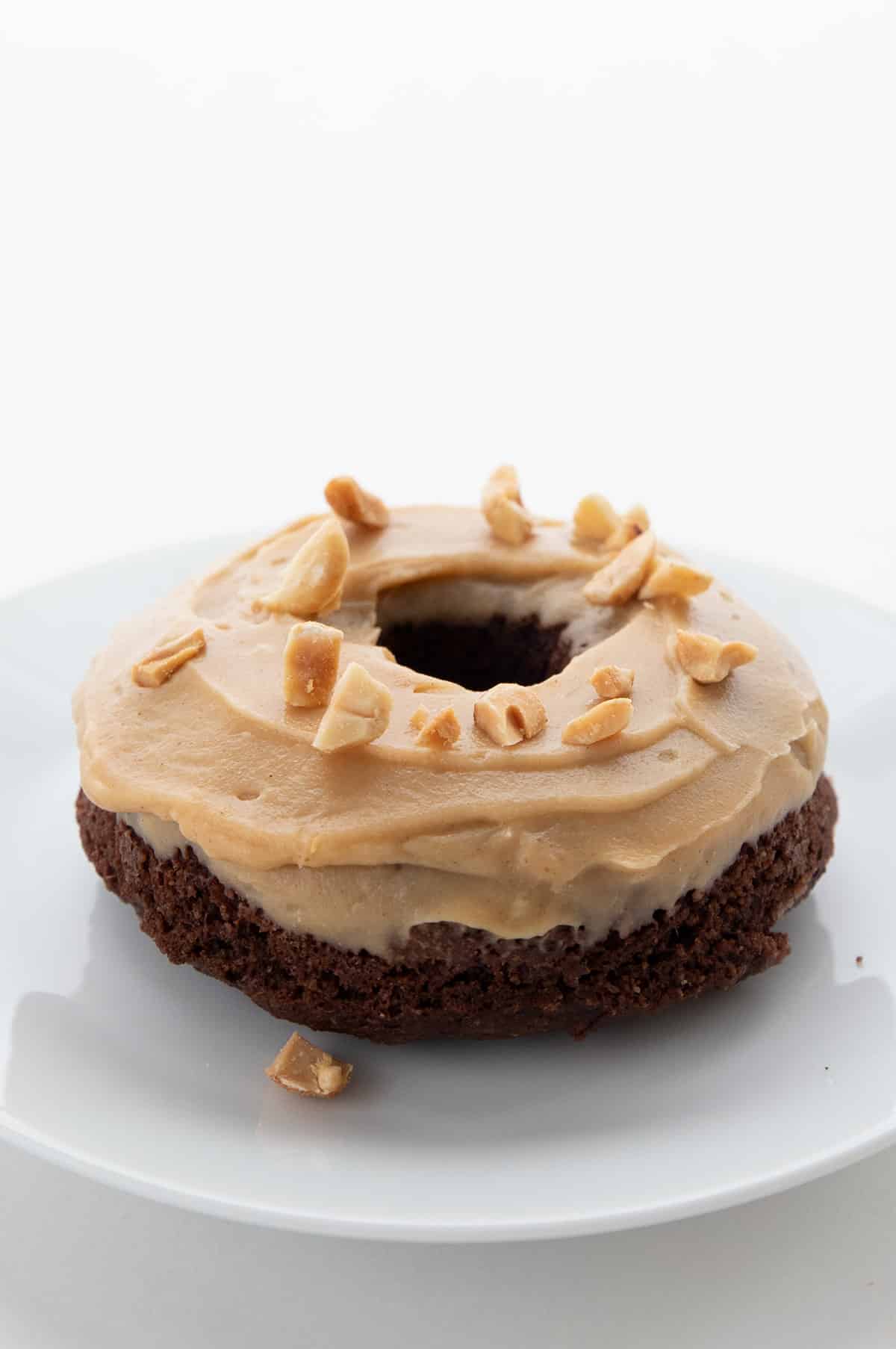 A keto chocolate donut with peanut butter glaze on a white plate.