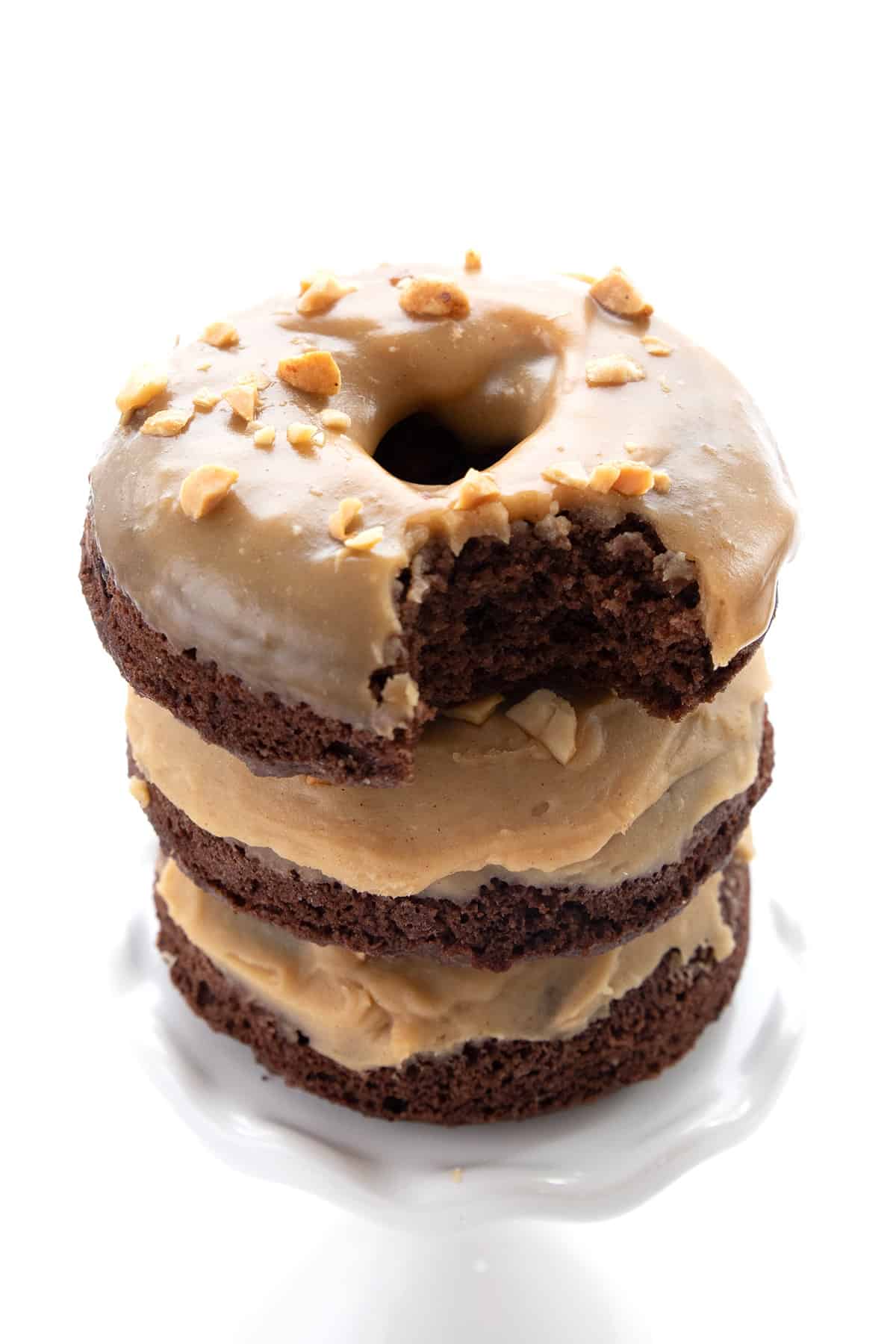 A stack of Keto Chocolate Peanut Butter Donuts on a white cupcake stand, with a bite taken out of the top one.