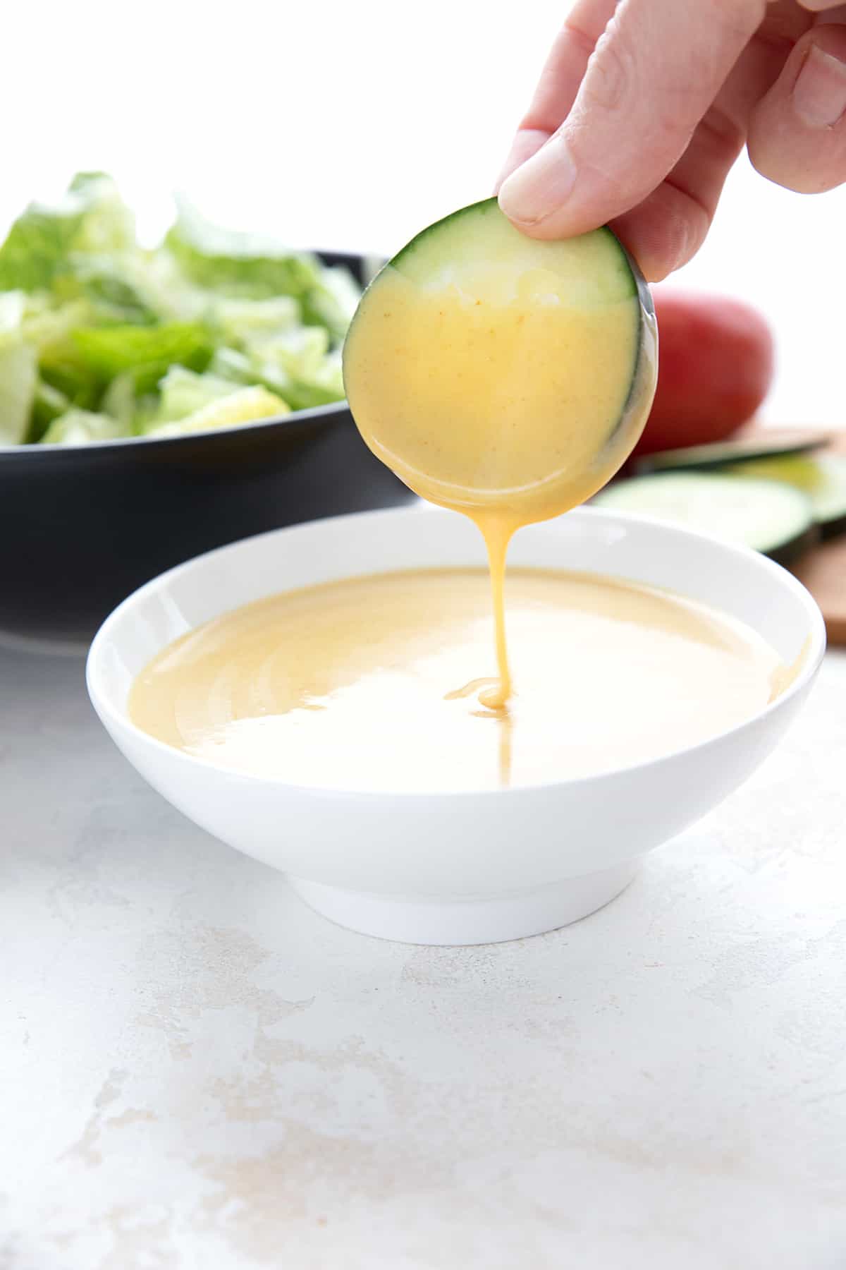 A slice of cucumber being dipped into honey mustard sauce in a white bowl.