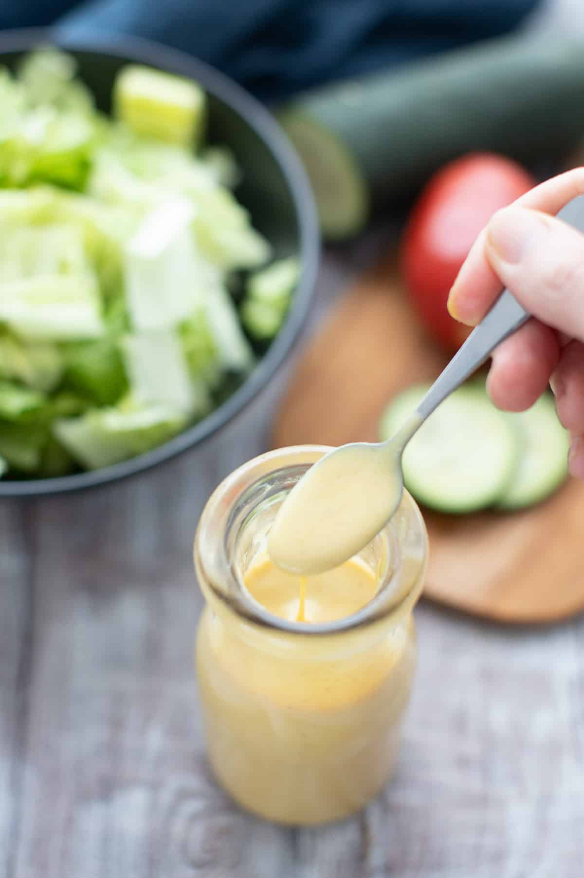 Keto honey mustard dressing in a glass bottle with salad makings around it.
