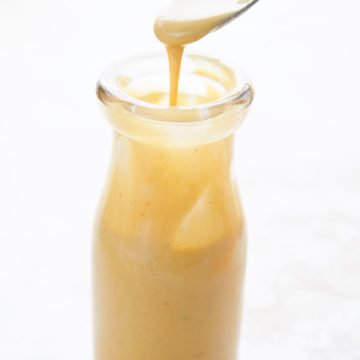 A spoon drizzling sugar free keto honey mustard into a glass bottle.