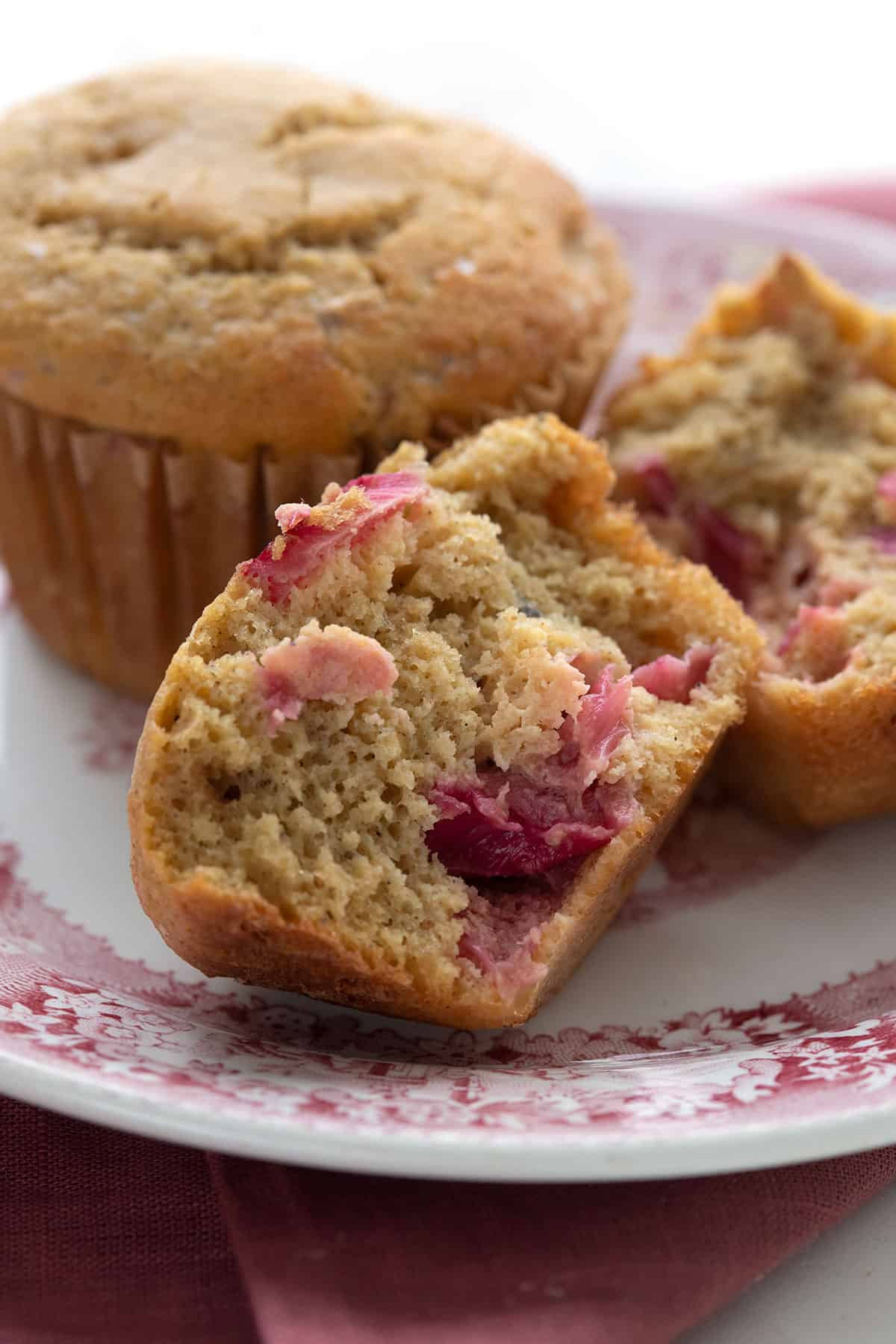 Close up shot of a keto rhubarb muffin, broken open, on a red patterned plate.